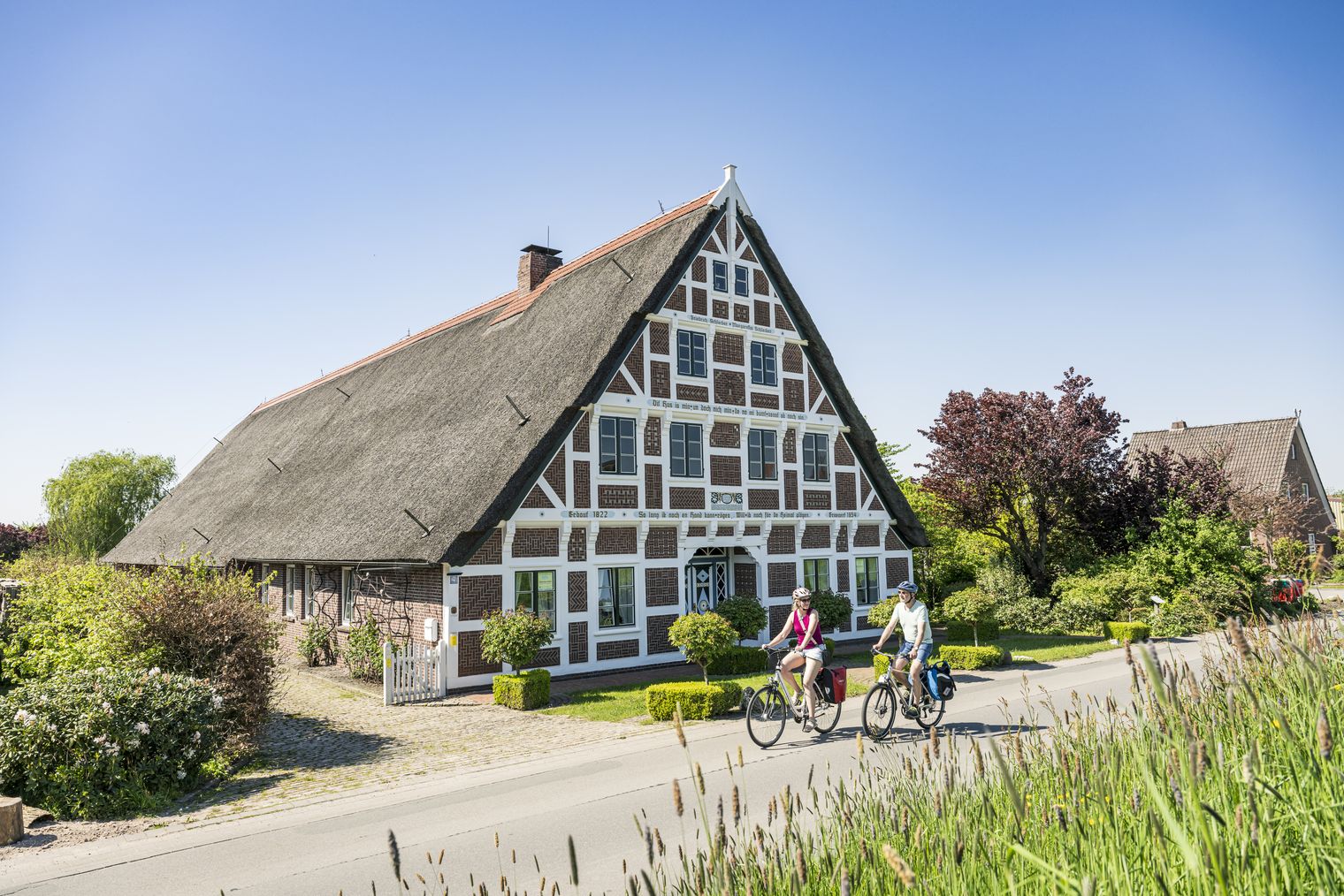 Mann und Frau fahren auf Fahrrädern an einem Fachwerkhaus im Alten land vorbei